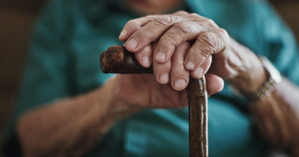 close up of an elderly woman's hands resting on a walking cane