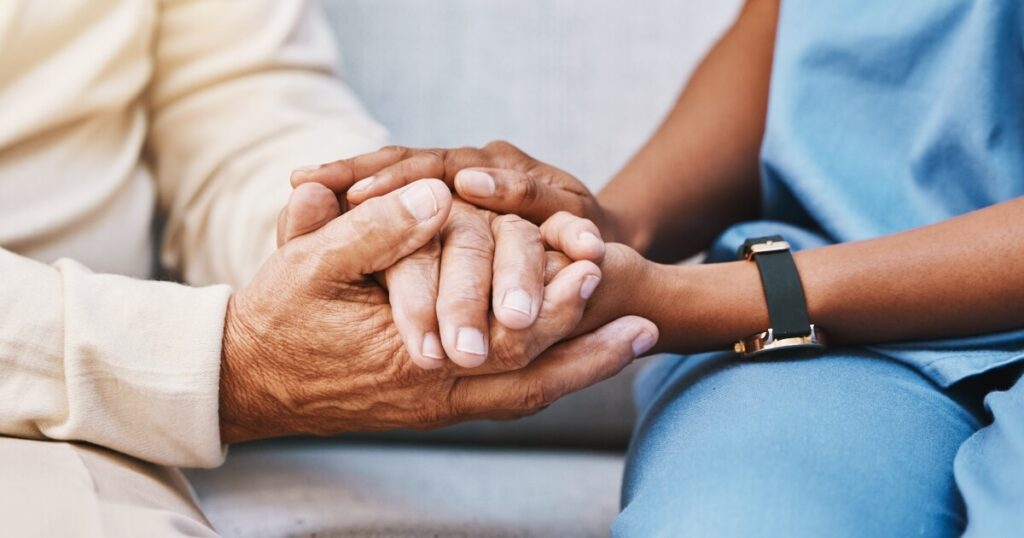 closeup of a caregiver holding the hands of an elderly patient