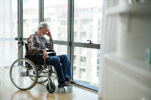 elderly man sitting alone in wheelchair and looking out window