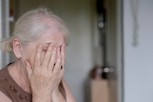 Elderly woman in nursing home covering her face with her hands.