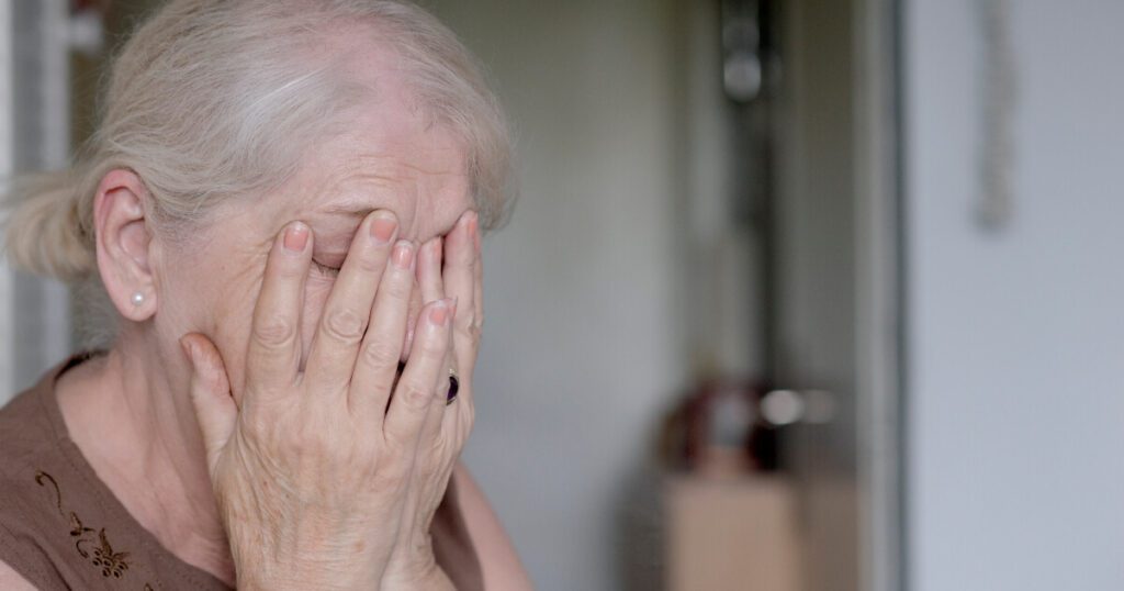 Elderly woman in nursing home covering her face with her hands.