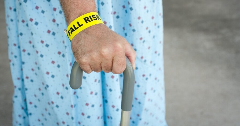 close-up side view of elderly man's hand holding a cane wearing hospital robe